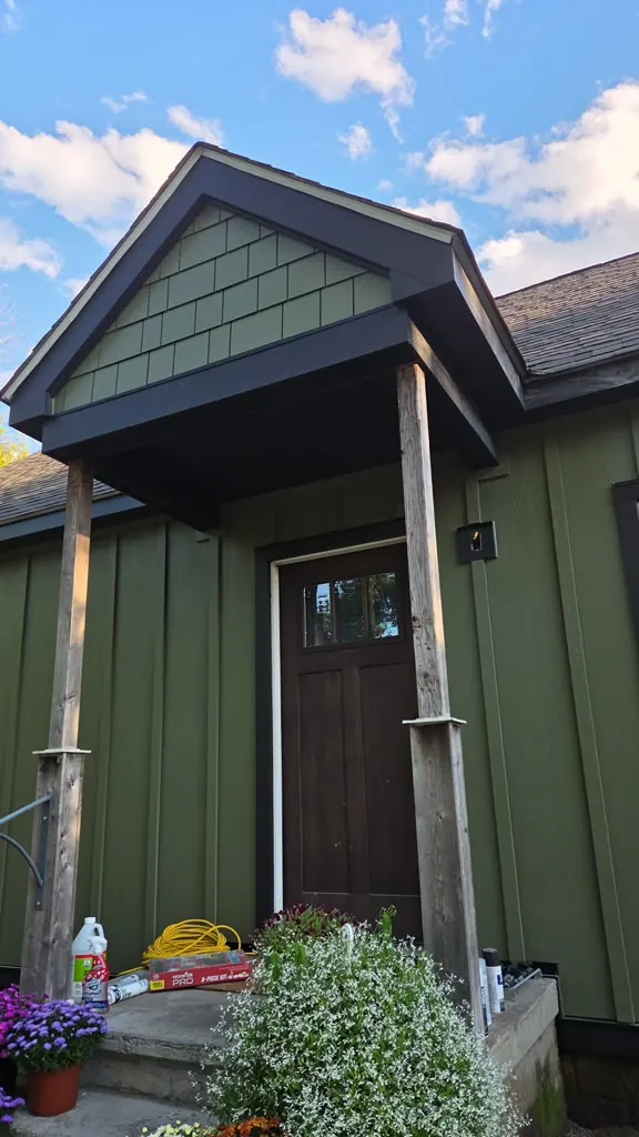 Completed olive green board and batten siding with a cedar shake gable entry portico