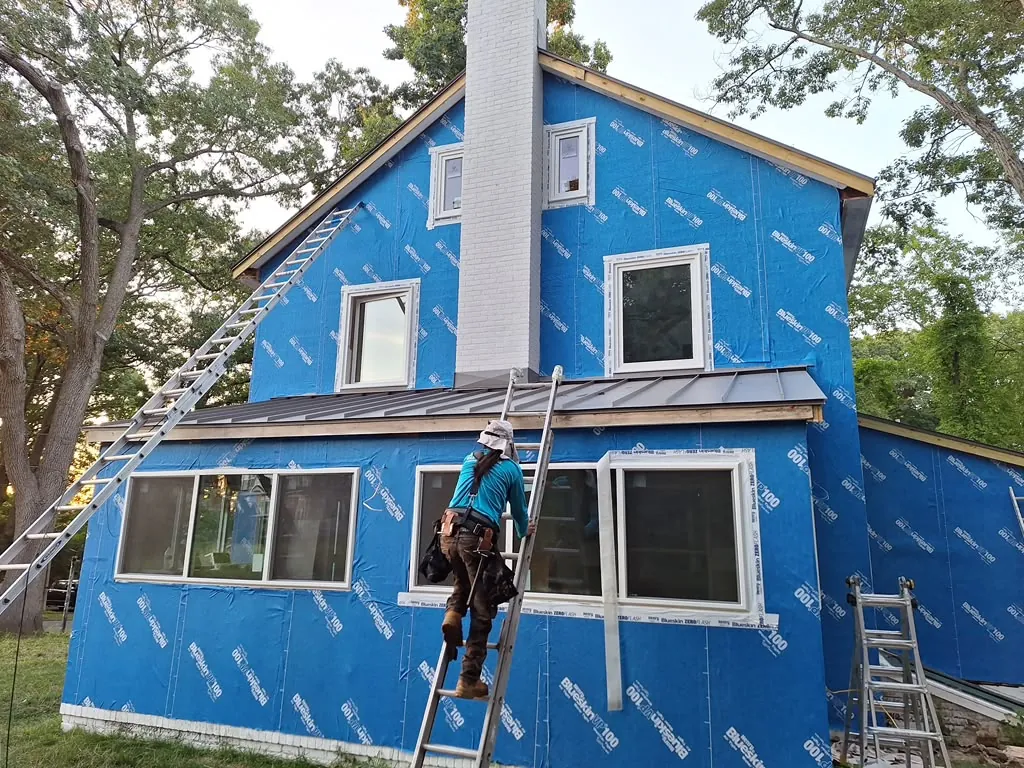 Standing-seam metal roof section and siding installation around a brick chimney