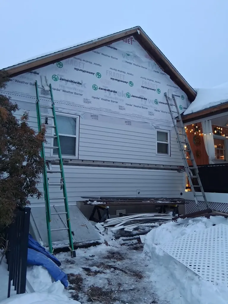 Crew member on a ladder installing white board and batten siding on a gable