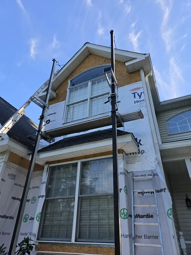 Siding installation in progress with house wrap and ladder jacks