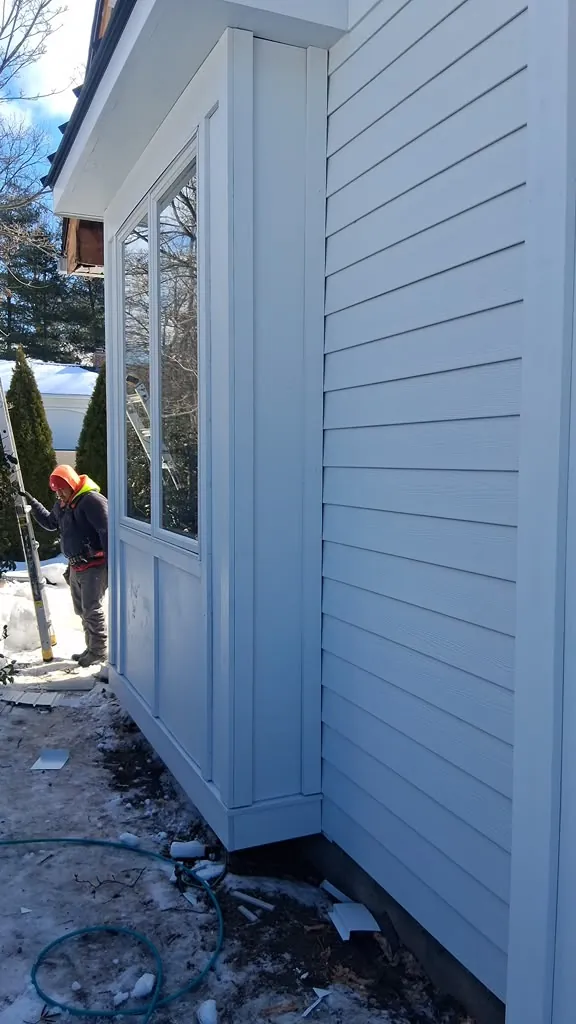 Crew member on a ladder installing board and batten siding in the snow